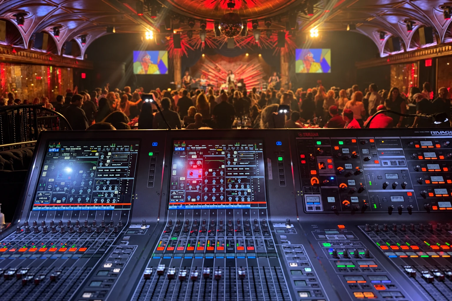 A live sound mixing console overlooking the audience and stage at a music venue
